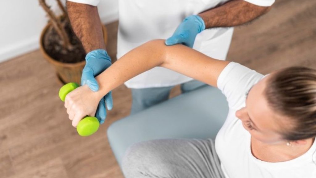 Physiotherapist guiding a patient through a forearm and elbow strengthening exercise using a dumbbell.