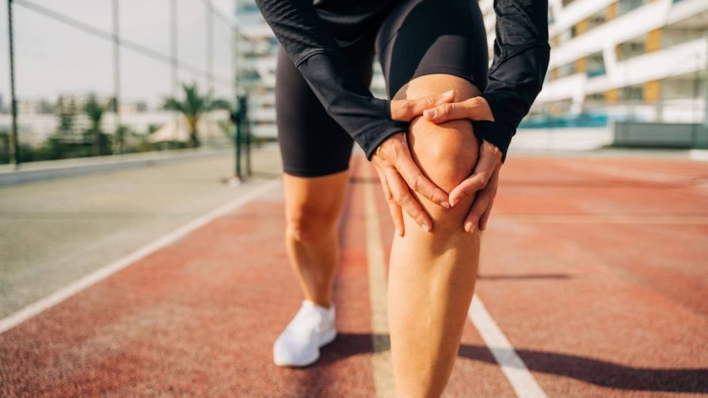 Runner holding their knee in pain during training on a running track.