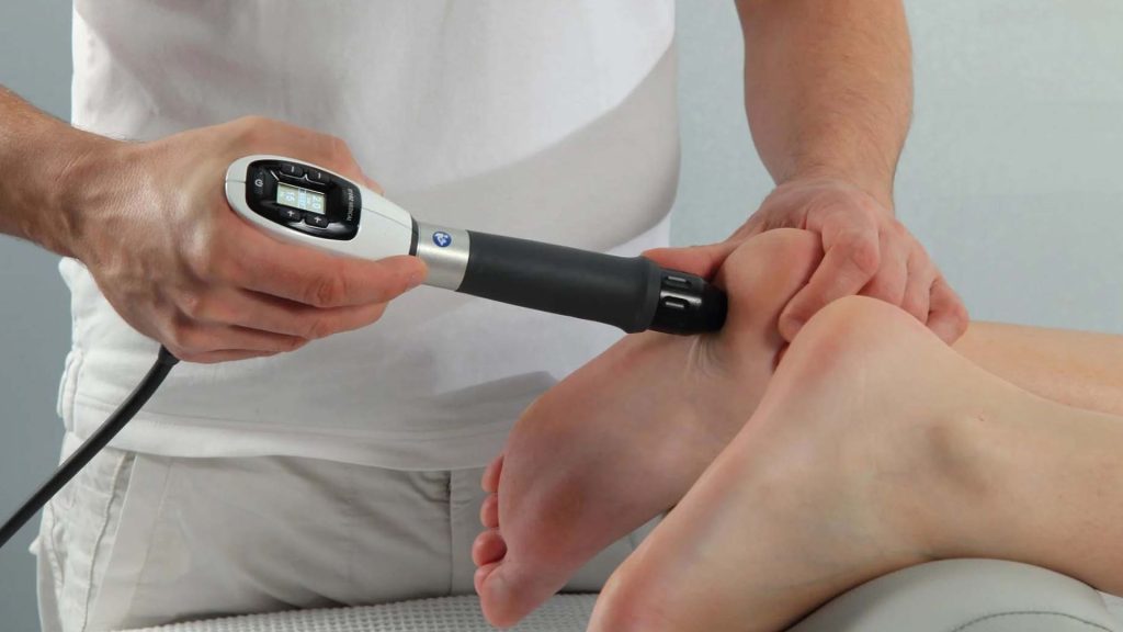 Physiotherapist applying shockwave therapy to a patient’s heel using a handheld device, commonly used to treat tendon-related pain such as plantar fasciitis and Achilles tendinopathy.