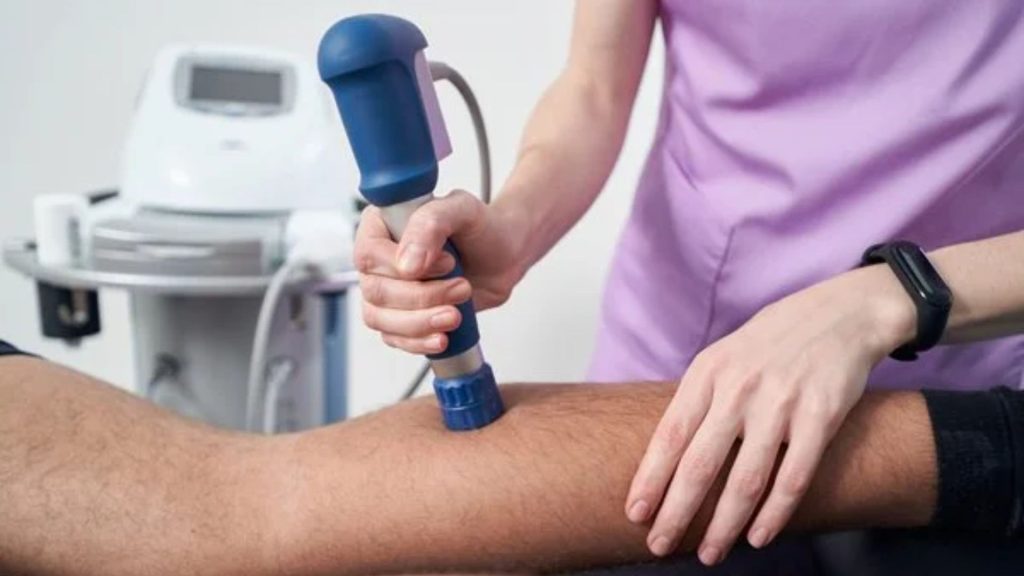 Physiotherapist delivering shockwave therapy to a patient’s lower leg using a handheld device, targeting tendon and muscle tissue to support healing in chronic overuse injuries.