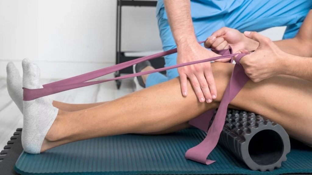 Physiotherapist guiding a patient through rehabilitation exercises using a resistance band and foam roller to restore strength, control, and movement as part of a structured physiotherapy programme.