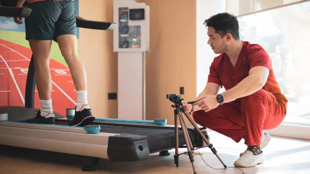 Physiotherapist recording a runner on a treadmill for detailed gait analysis in a clinic.
