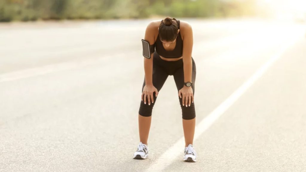 Runner resting with hands on knees in the middle of her running session, showing fatigue and the need for recovery planning.