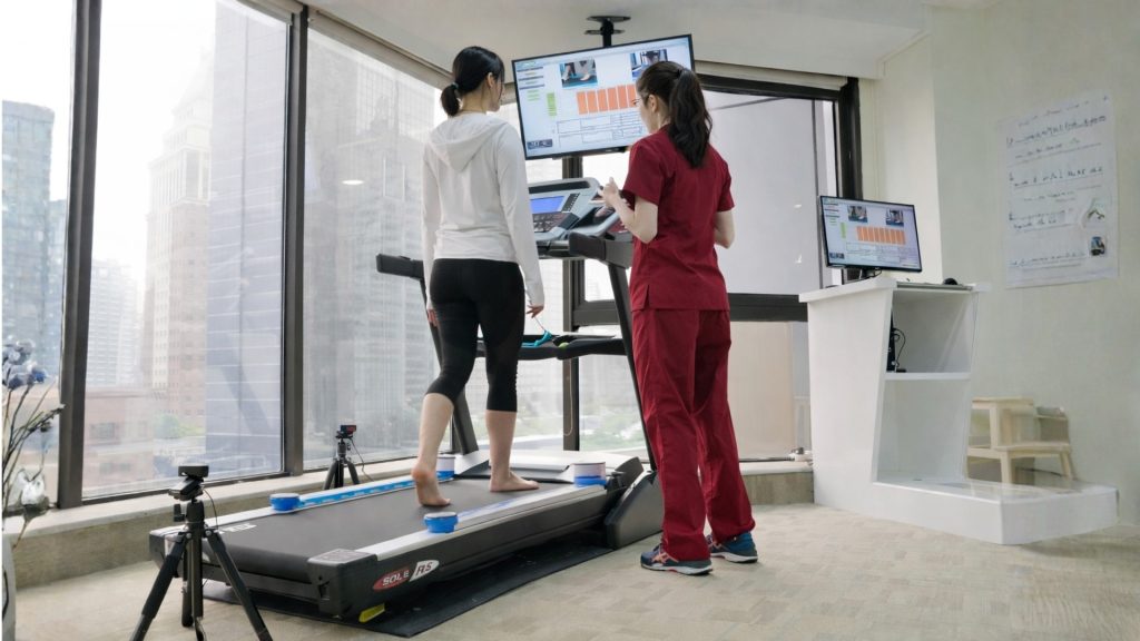 Physiotherapist guiding a runner through treadmill gait analysis using motion tracking equipment.
