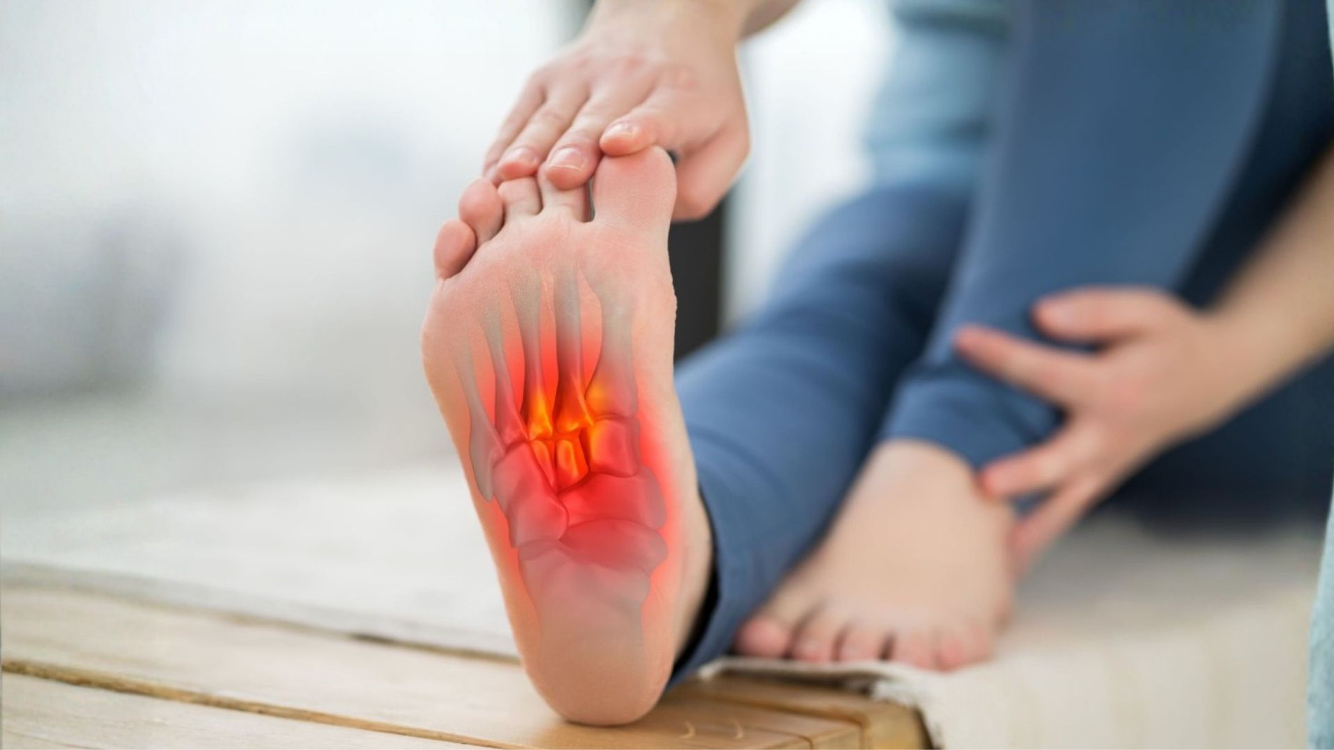 Close-up of a person holding their foot with a red highlighted area on the heel, illustrating plantar fasciitis and heel pain on the sole of the foot.