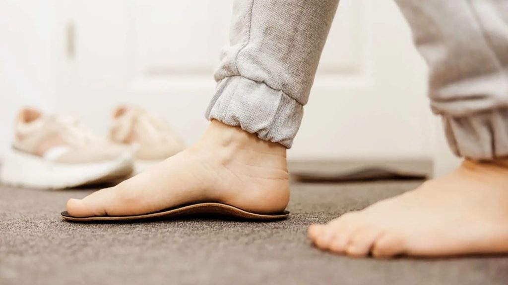 Person standing on a custom insole at home, showing foot arch support during daily activity.
