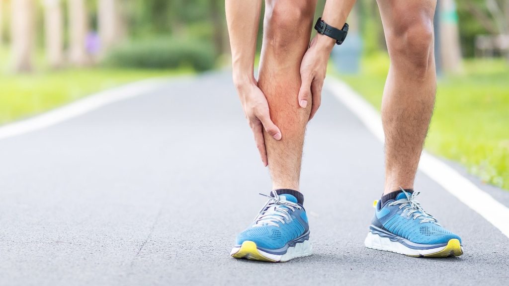 Runner holding the lower leg, representing shin pain and shin splints caused by repetitive impact from running