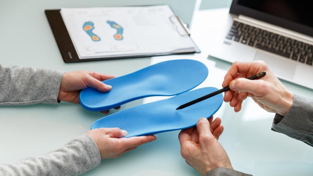Podiatrist reviewing and explaining custom insoles during a foot assessment consultation.
