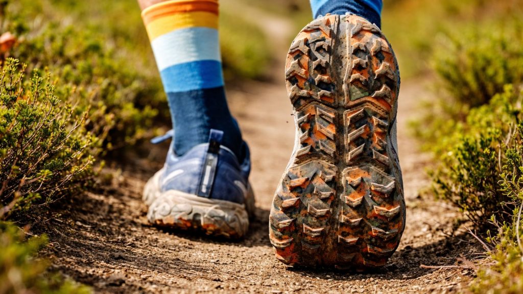 Trail running shoes mid-stride on a dirt path, showing repeated toe impact and pressure that can contribute to nail trauma in runners.
