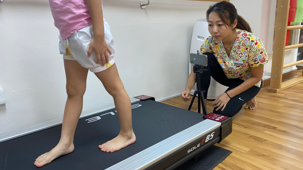 Podiatrist observing a child walking barefoot on a treadmill during a gait assessment, evaluating foot posture and movement.