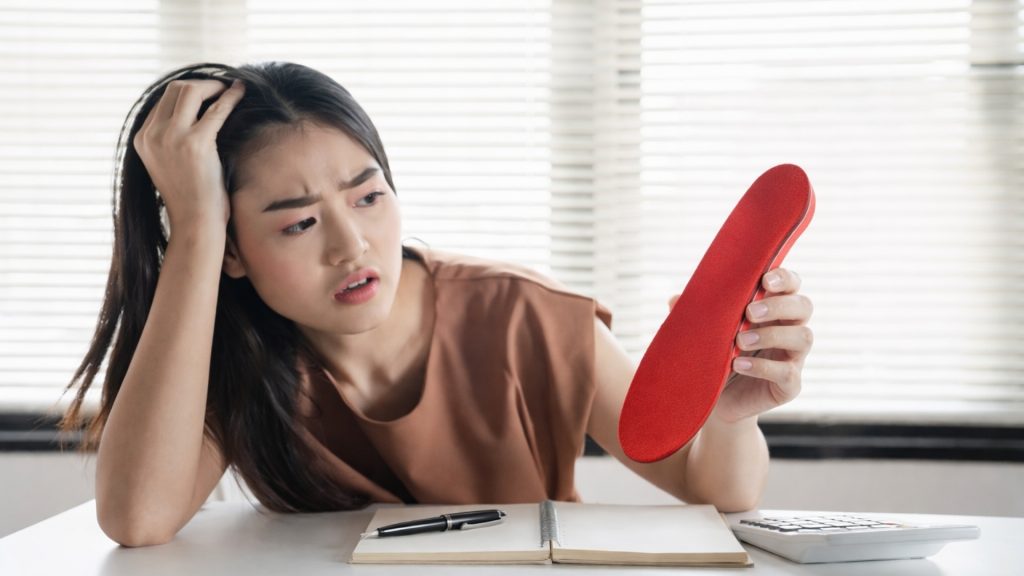 Person examining a custom insole with a confused expression, questioning whether custom insoles are worth it.