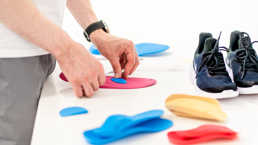 Podiatry professional customising orthotic insoles with support components next to running shoes.