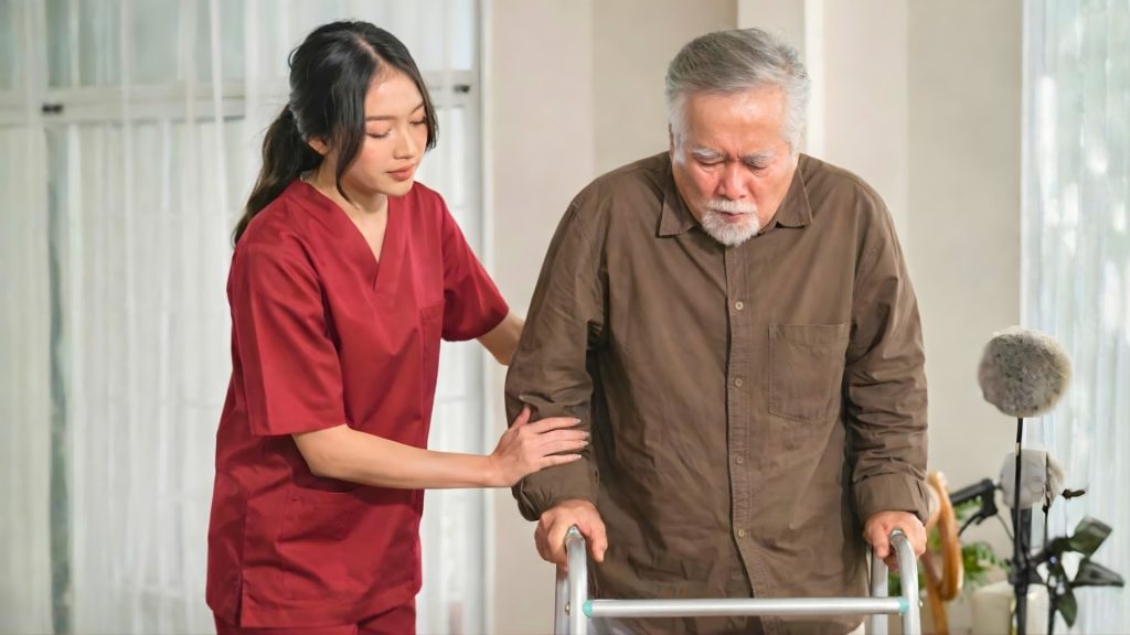 Physiotherapist assisting an elderly man walking with a frame during rehabilitation.
