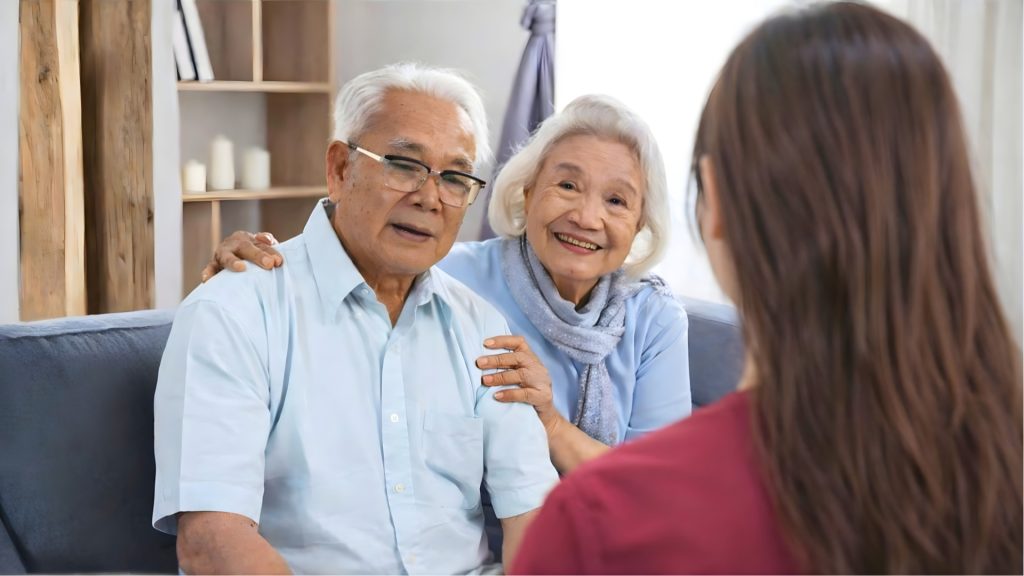 Elderly couple consulting a physiotherapist about musculoskeletal pain management and mobility support in a home setting.
