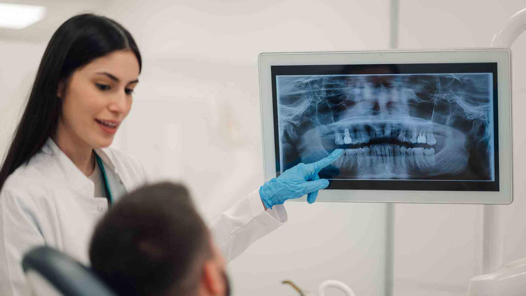 Dentist explaining jaw X-ray to patient, showing temporomandibular joint and teeth alignment.