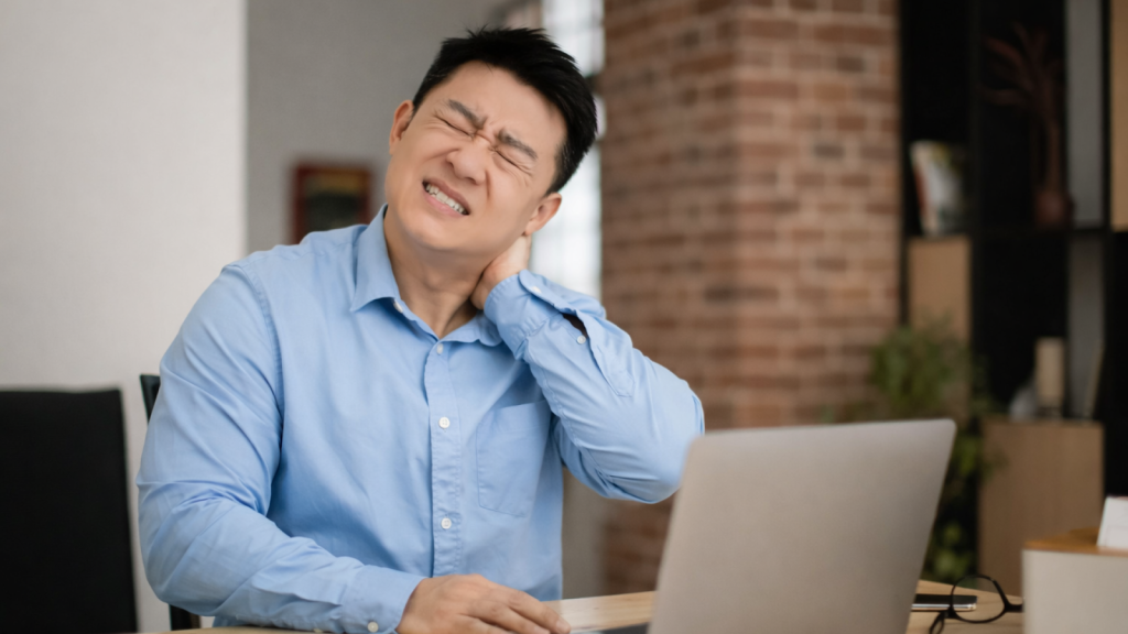 Asian office worker experiencing sharp neck pain while working on laptop at desk