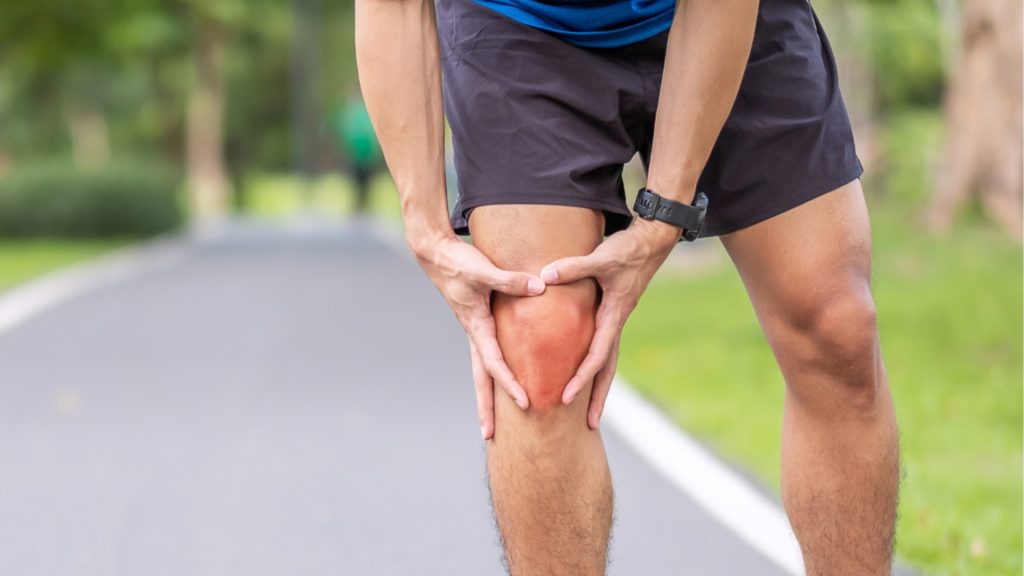 Close-up of runner holding painful knee outdoors, indicating ligament strain or ACL injury.
