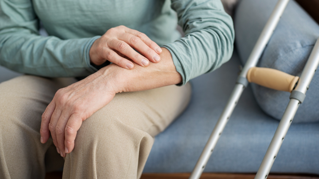Senior person sitting on a sofa holding their forearm in discomfort, with a walking cane resting beside them.