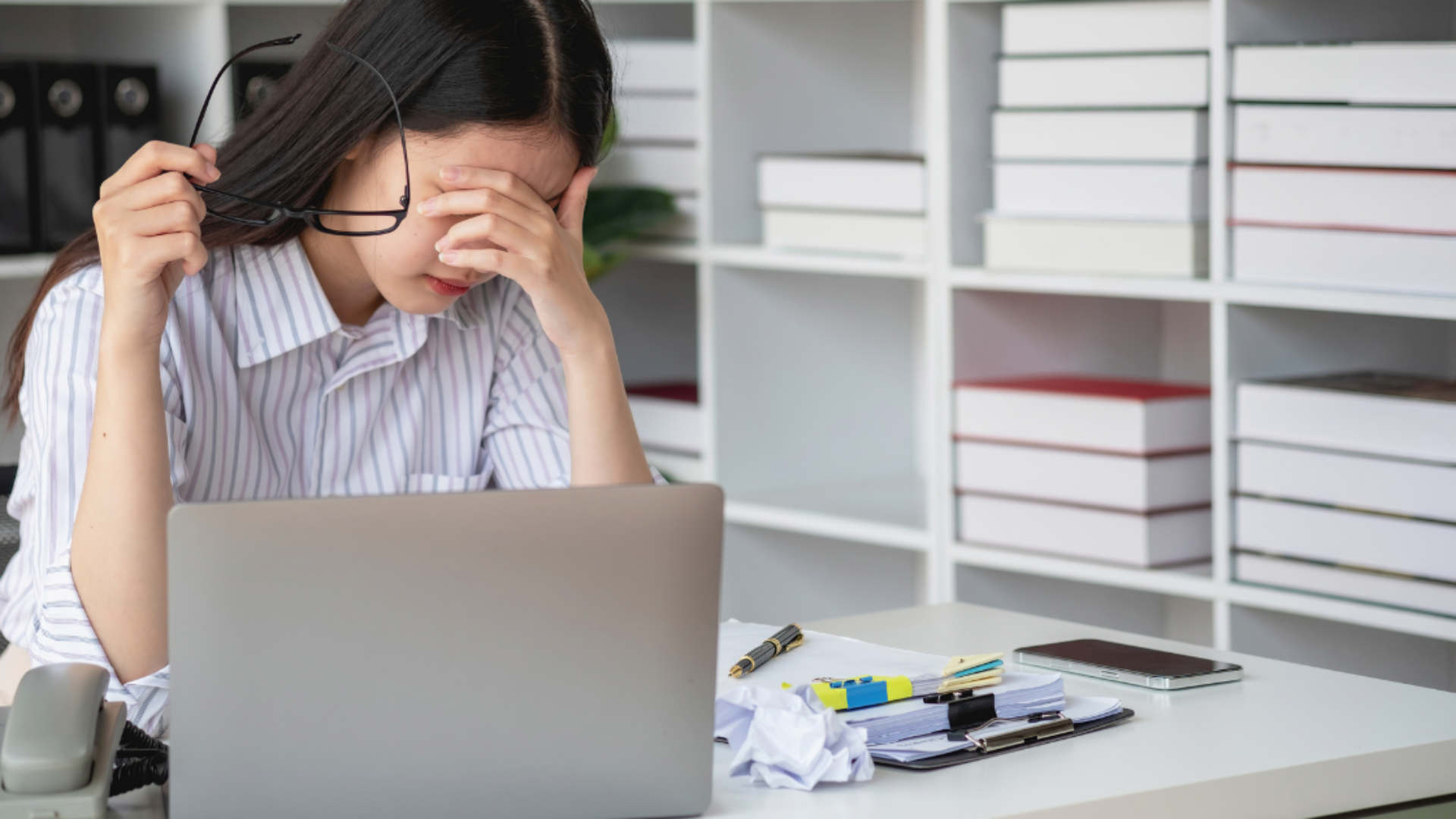 Office worker holding head in pain while working on laptop, illustrating tension headache from desk work