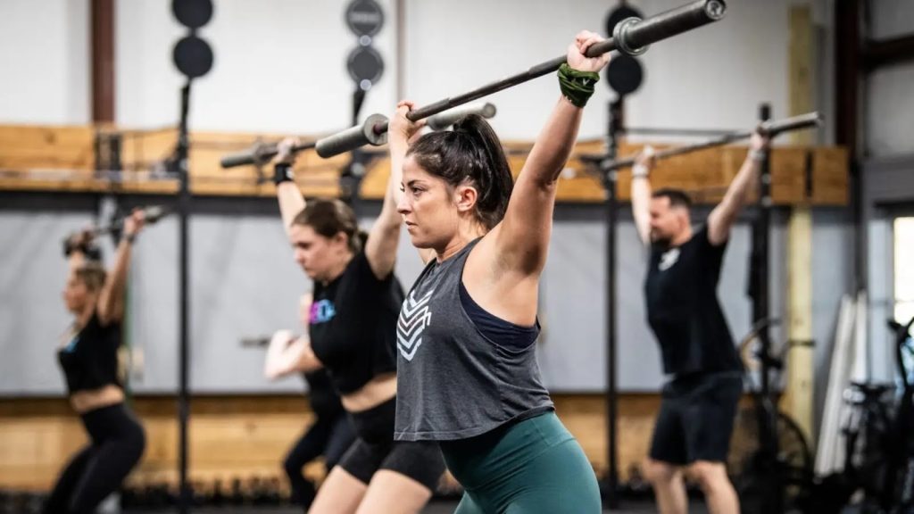 Group fitness class doing overhead barbell lifts in the gym.
