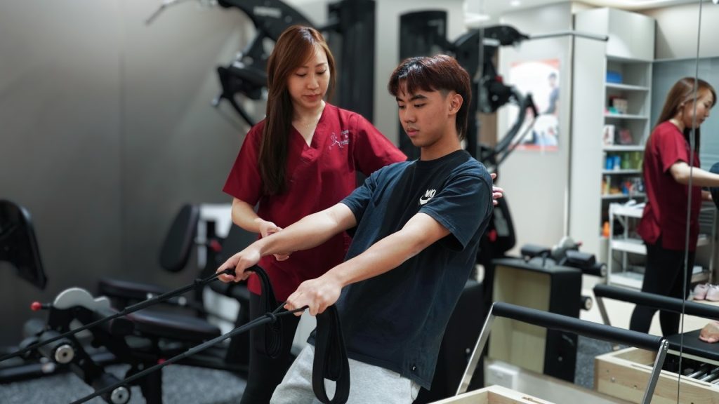 Physiotherapist guiding patient through resistance band pulling exercise in rehabilitation gym.
