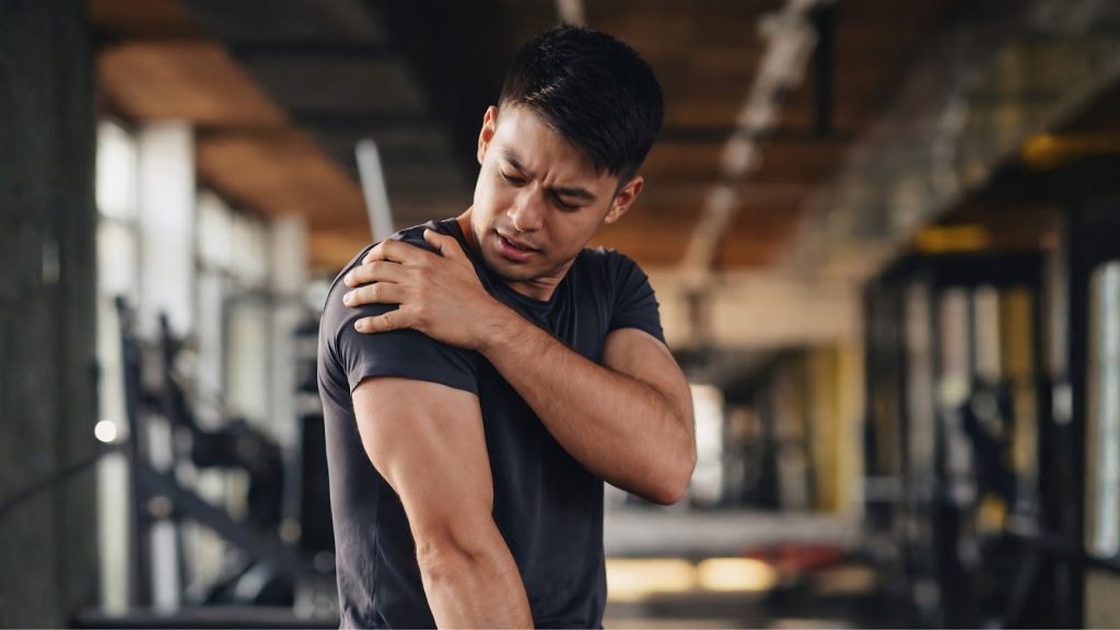 Man holding shoulder in pain after workout, indicating muscle soreness.
