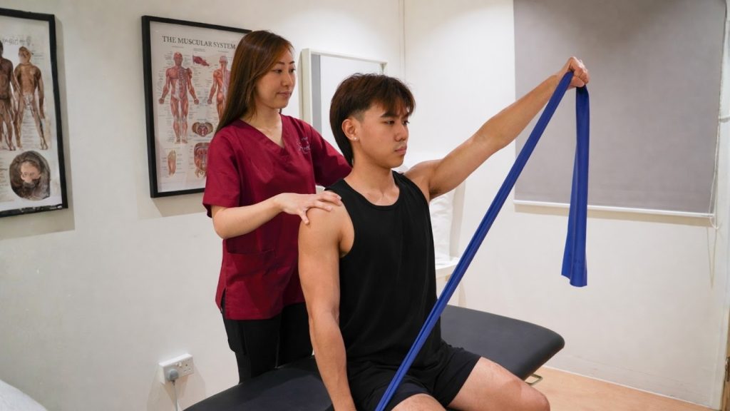 Physiotherapist assisting patient with resistance band shoulder exercise.
