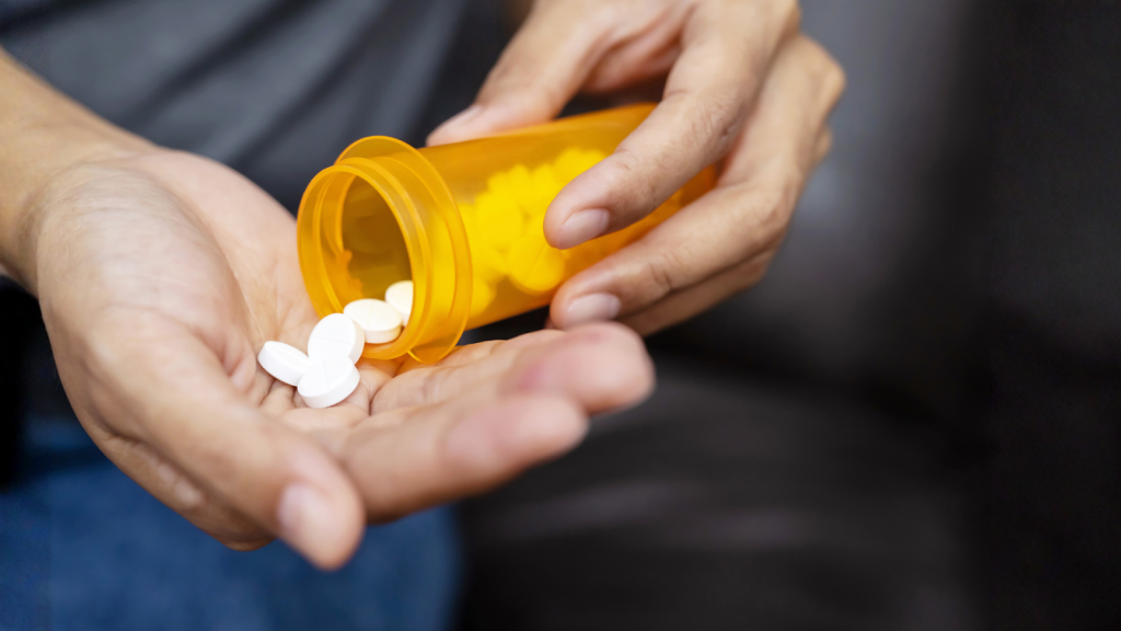 Person pouring painkiller tablets from orange prescription bottle into hand, representing temporary relief for sciatica or lower back pain