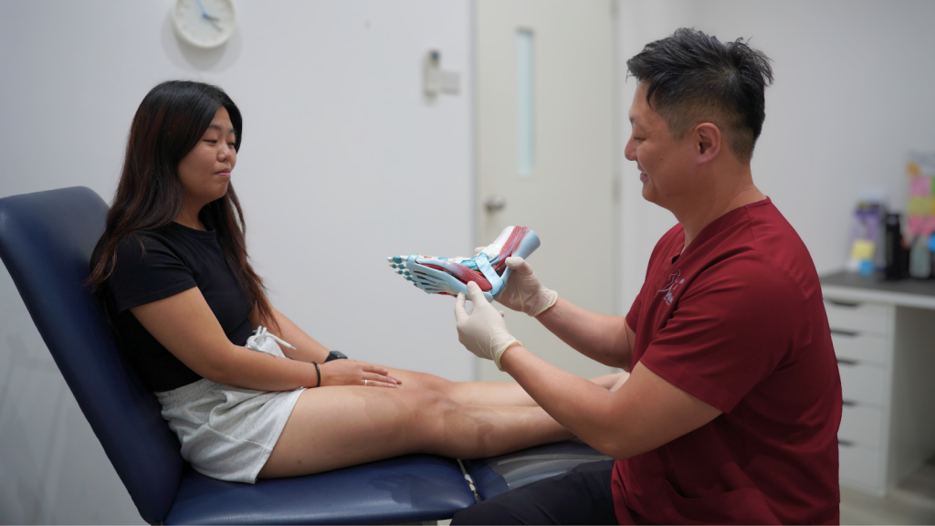Podiatrist explaining plantar fascia and foot structure using an anatomical model during a consultation with a patient experiencing heel pain