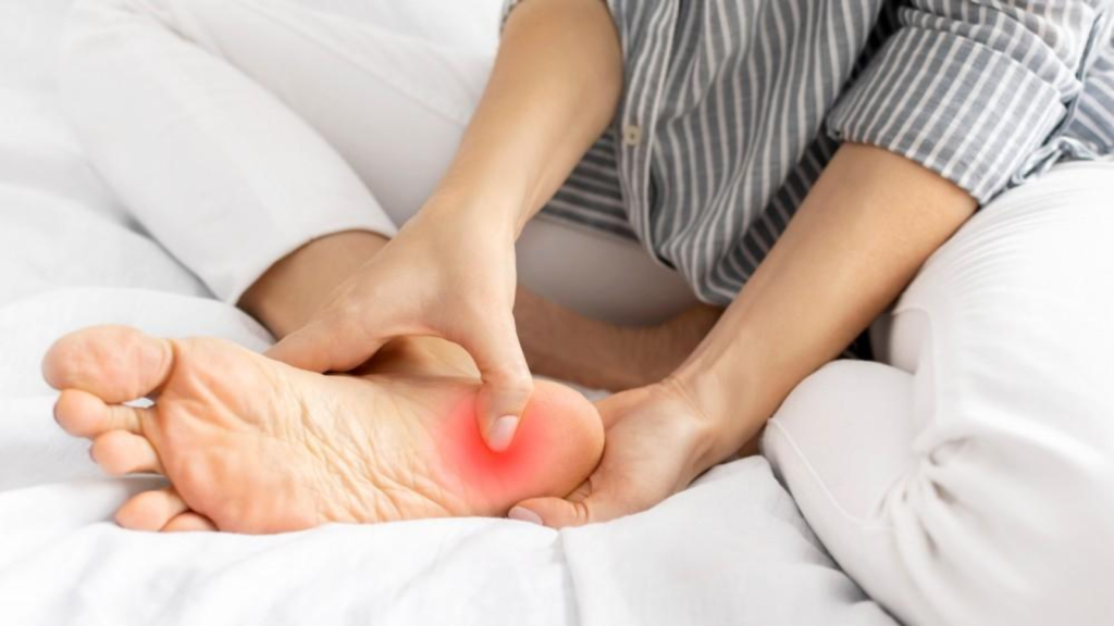 Person massaging the heel while sitting on a bed, highlighting plantar fasciitis pain during rest or after inactivity