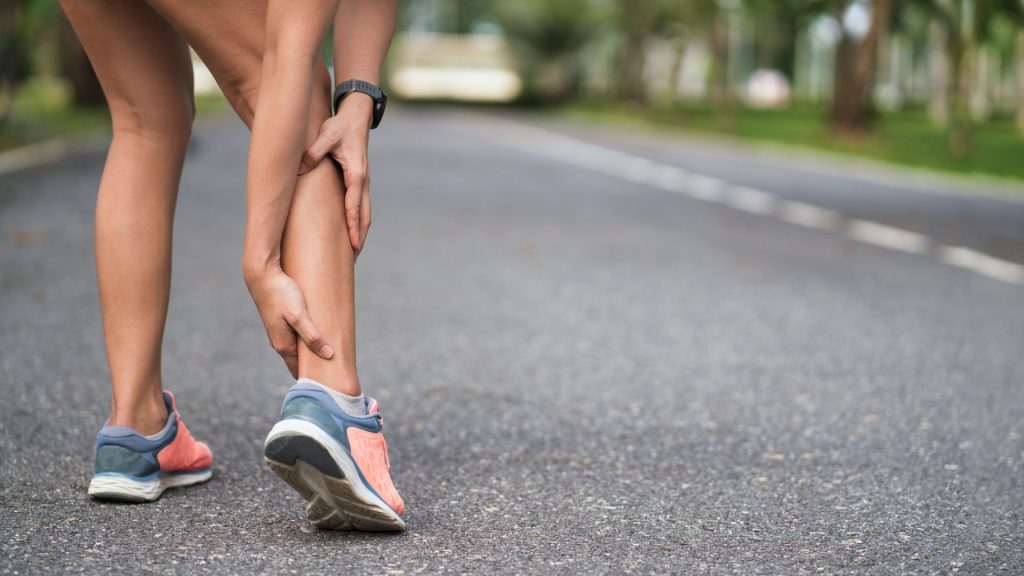 Runner holding lower leg in pain, showing symptoms of tendonitis from overuse.

