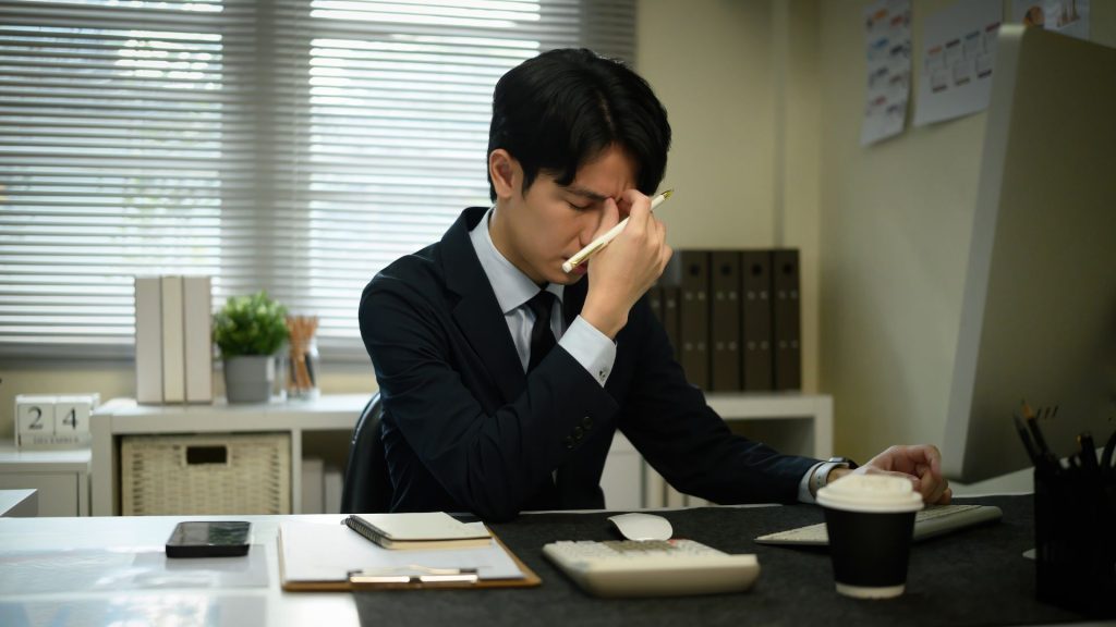 office worker with stress-related headache at desk possibly linked to neck tension treated with physiotherapy Singapore
