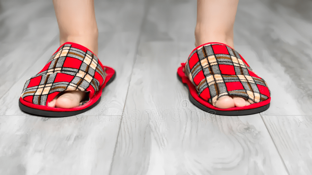 Person wearing flat soft indoor slippers on hard flooring, showing the type of unsupportive home slippers people with flat feet may need to avoid. 