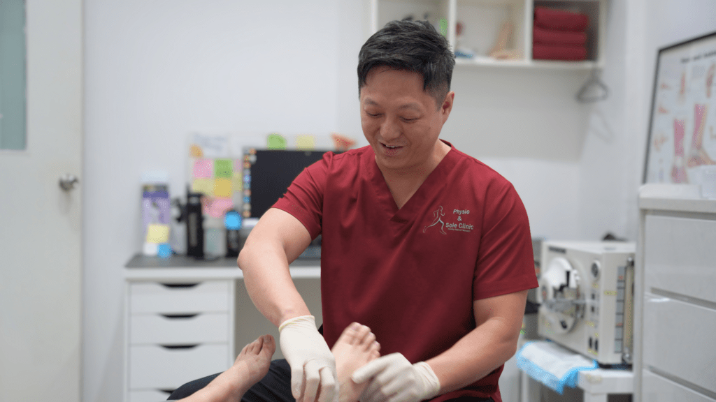Podiatrist in red scrubs examining a patient’s foot during a podiatry assessment for morning stiffness and possible plantar fasciitis. 