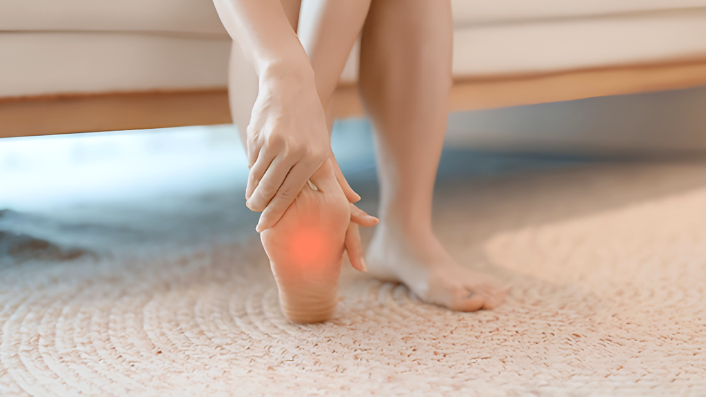 Person holding the bottom of their heel at home, showing plantar fasciitis-related heel pain and foot strain.