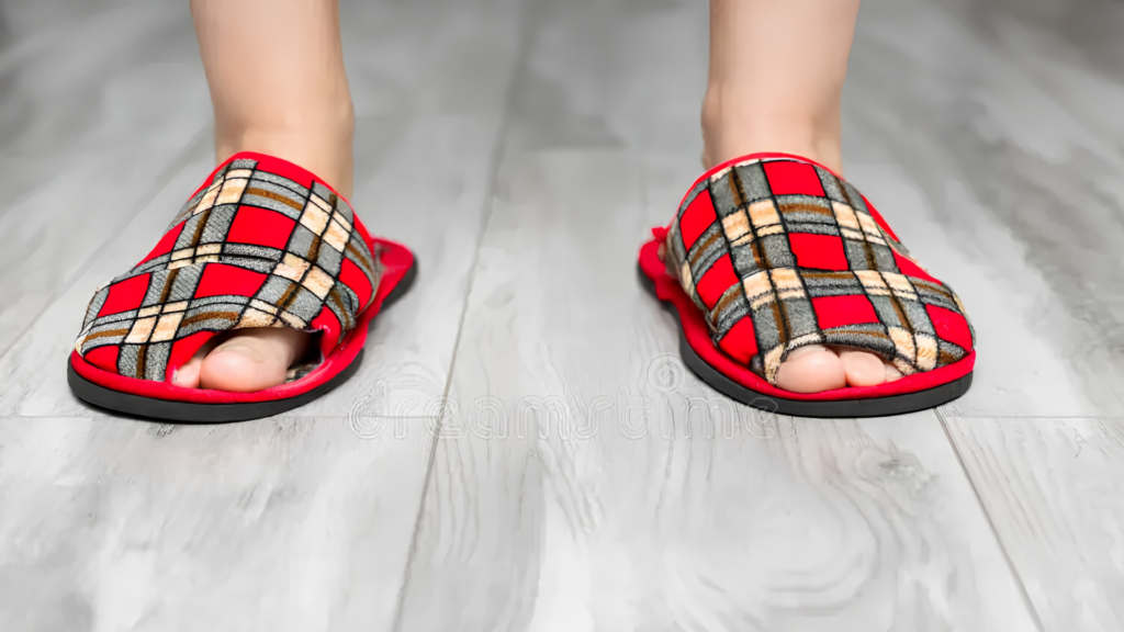 Person wearing flat soft indoor slippers on hard flooring, showing the type of unsupportive home slippers people with flat feet may need to avoid. 
