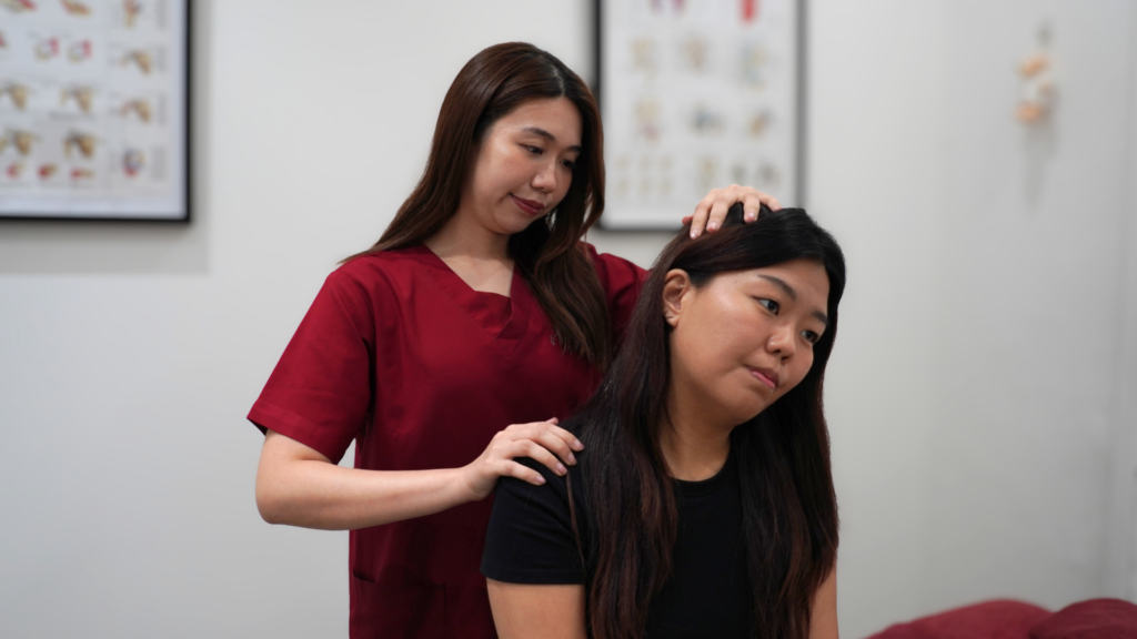 Physiotherapist in red scrubs assessing neck mobility of patient during a sports massage therapy session  